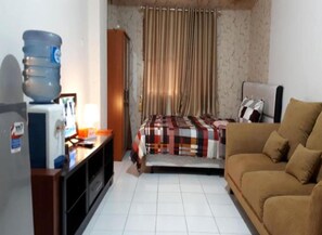 A compact hotel room with a bed, a sofa, a desk with a computer, and a water dispenser. - Apartmen City Park by GC Realty by Zuzu (Jakarta)