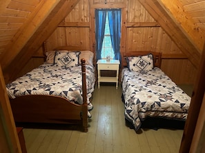 Un dormitorio acogedor en el ático con dos camas de madera, una mesita de noche y una ventana con cortinas.