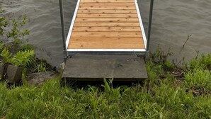 Een houten steiger die uitsteekt in een rustig meer, met een bebost heuvel op de achtergrond.