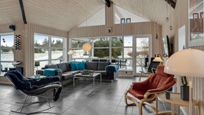 En rummelig opholdsstue med et stort vindue, en sofa, et sofabord og en gyngestol.