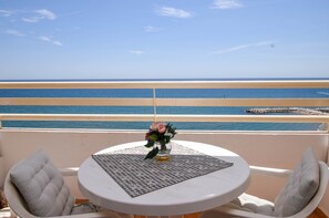 Un balcon avec une table et des chaises, donnant sur une plage avec une jetée.