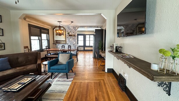 A spacious living room with a wooden floor, a blue armchair, a brown sofa, and a dining area with a wooden table and chairs.