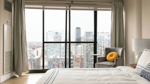 Une chambre d’hôtel avec une grande fenêtre, un lit, une chaise et une table de chevet.