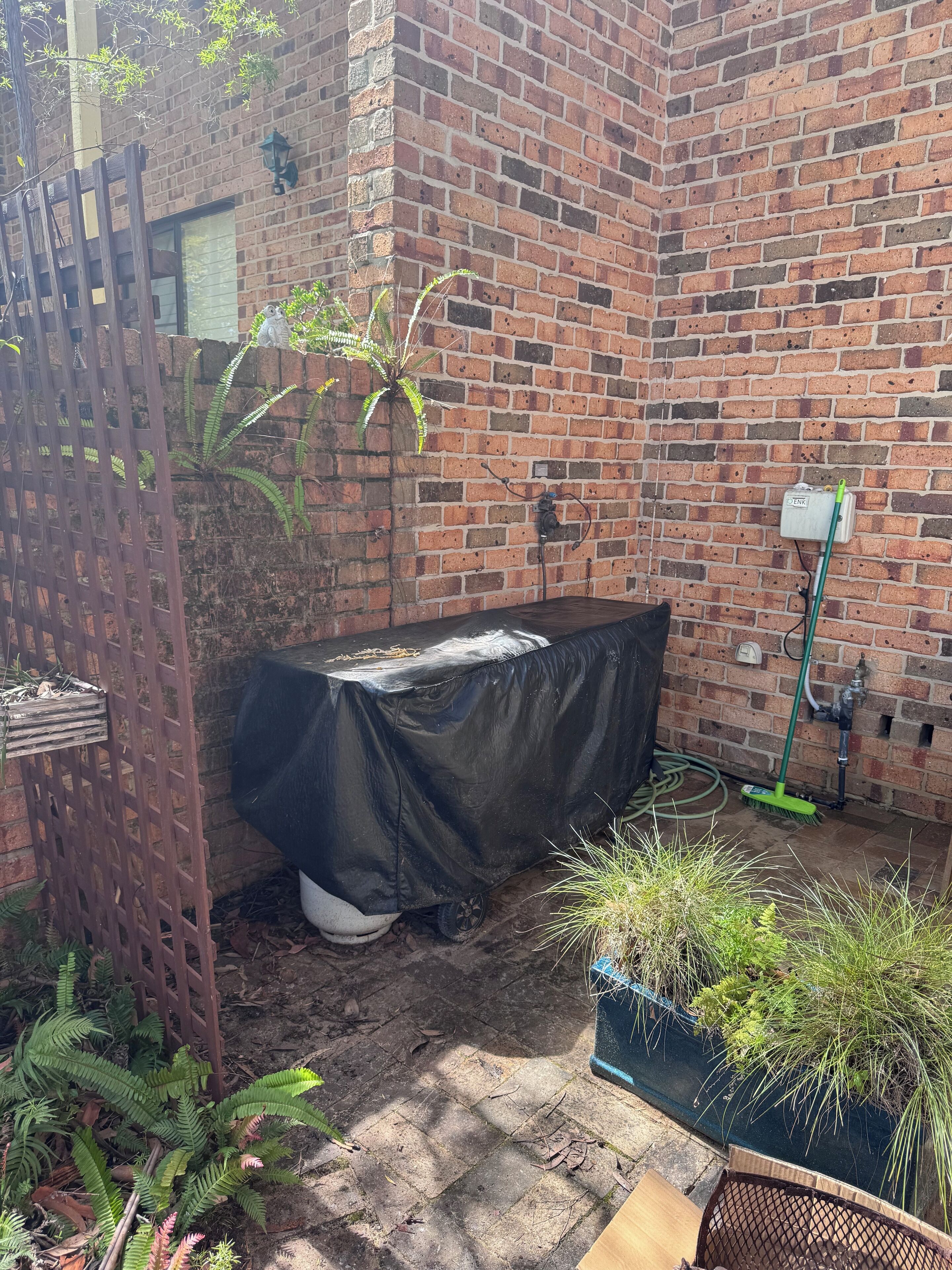 A brick wall with a water spigot, a covered table, and potted plants.