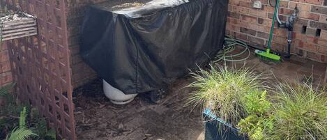 A brick wall with a water spigot, a covered table, and potted plants.