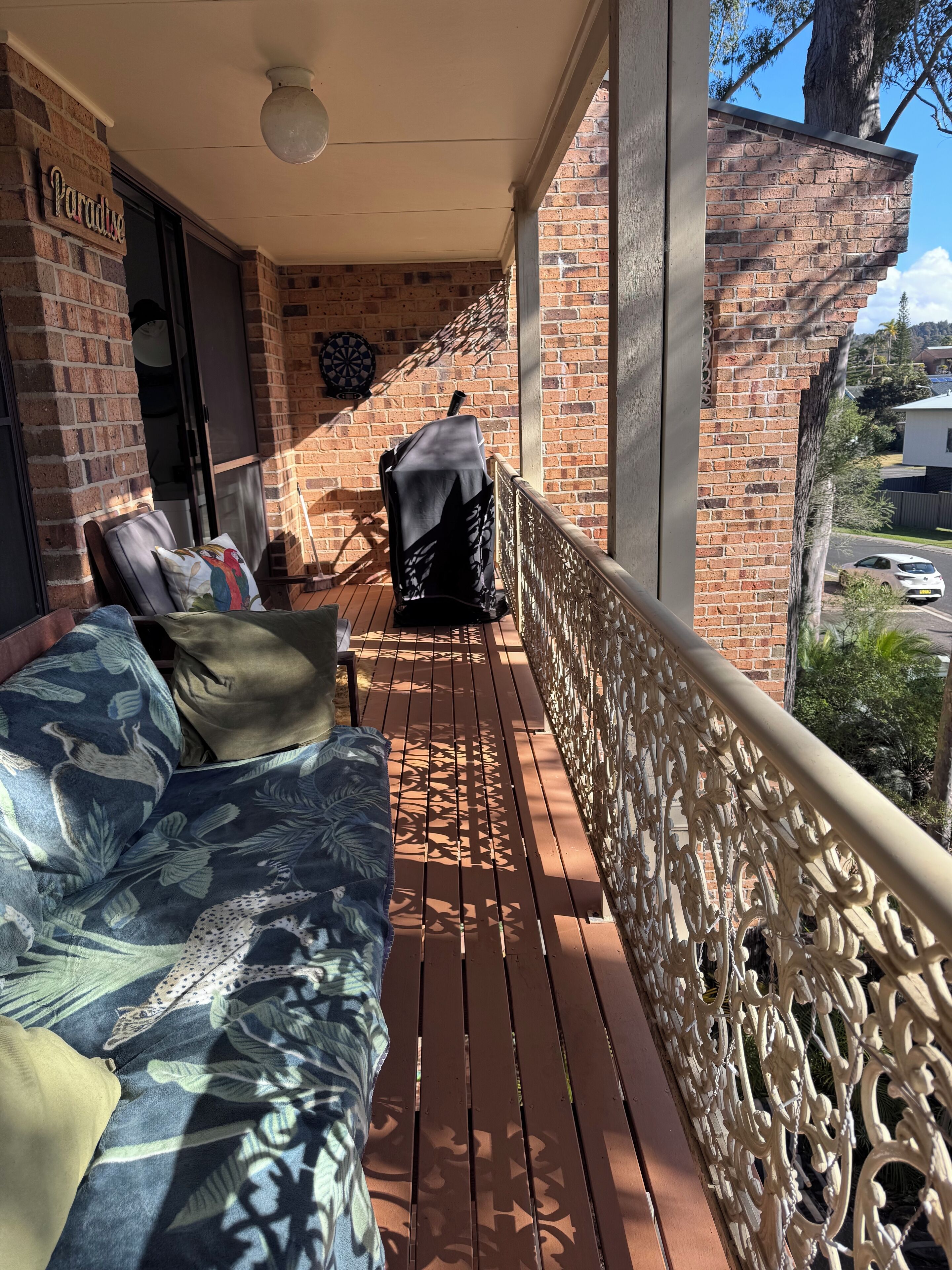 Ein überdachter Außenbereich mit Holzterrasse, eine überdachte Sitzgelegenheit mit Sofa und Sesseln sowie eine Ziegelwand mit Dartscheibe.
