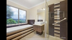 A modern bathroom with a large bathtub, a shower area with a glass door, and a window with a view of greenery. - Doreen Gem (Doreen)