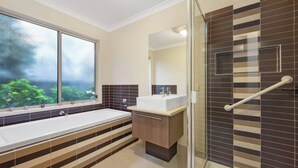 Un baño moderno con una bañera grande, una zona de ducha con puerta de cristal y una ventana con vistas a zonas verdes.