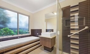 Ein modernes Badezimmer mit einer großen Badewanne, einer Duschkabine mit Glastür und einem Fenster mit Blick auf Grünflächen.