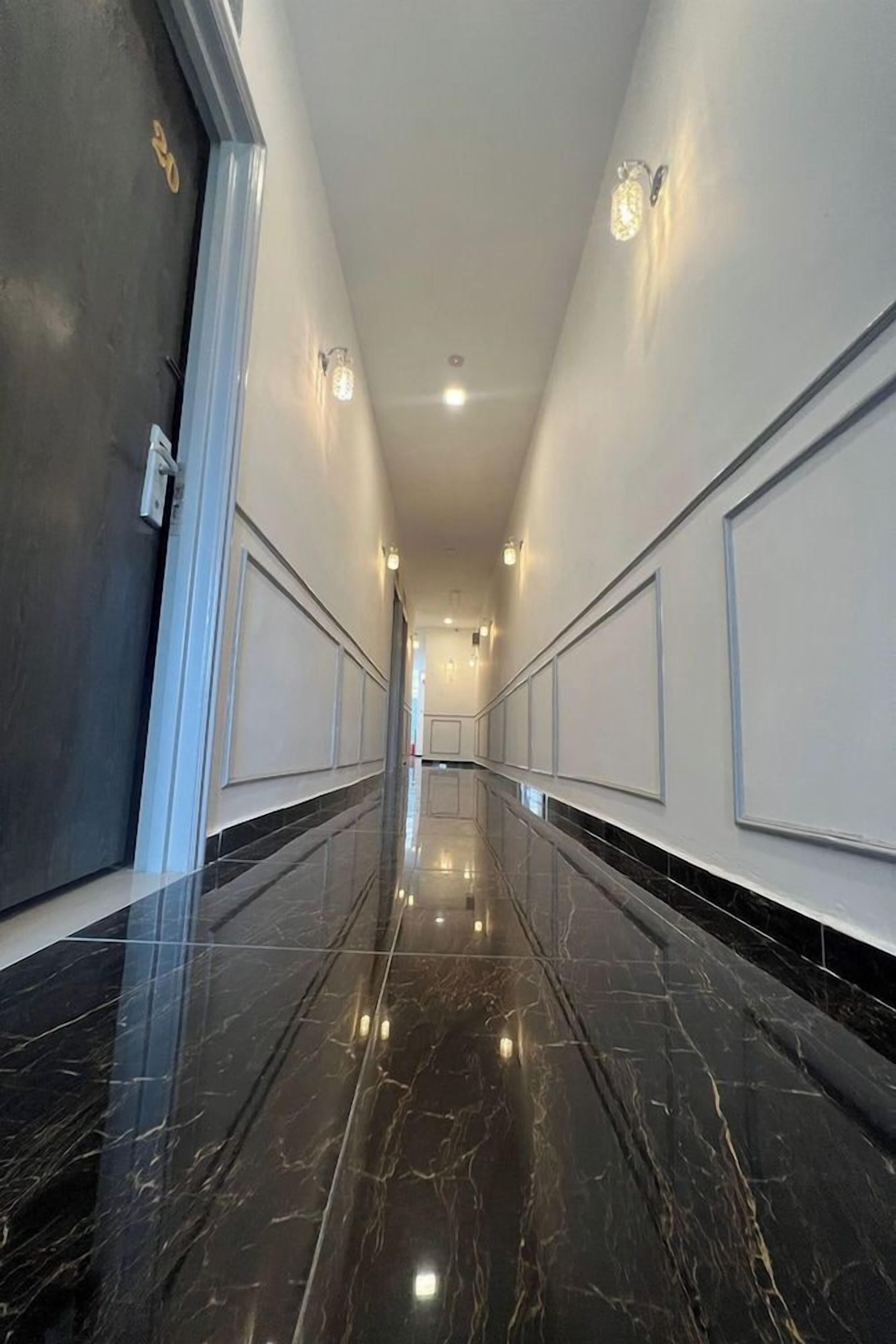 A corridor with a polished marble floor, white walls with paneling, and recessed lighting.