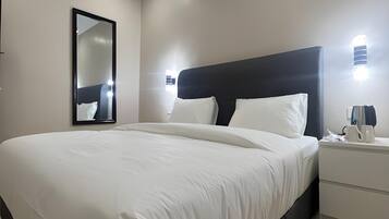 A hotel room with a large bed, a bedside table with a lamp, and a wall-mounted mirror.