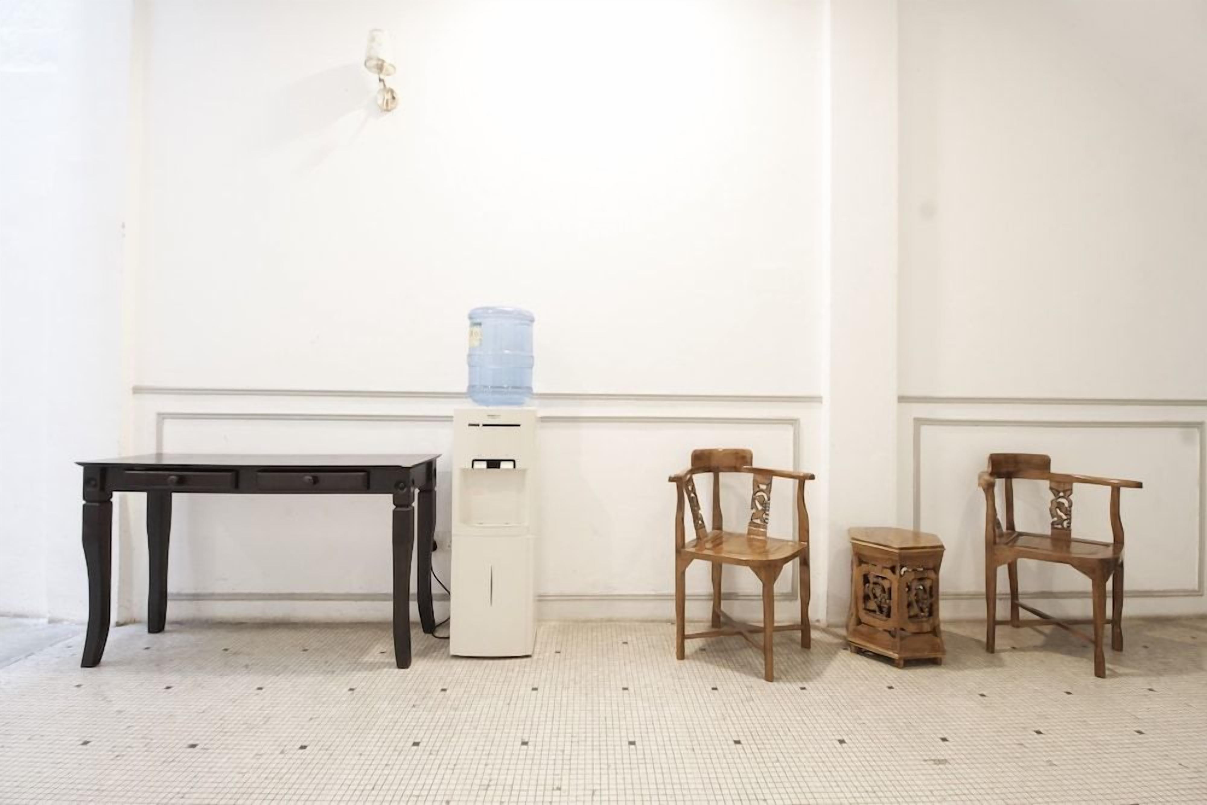 A room with a white wall, a water dispenser, a black table, and two wooden chairs.
