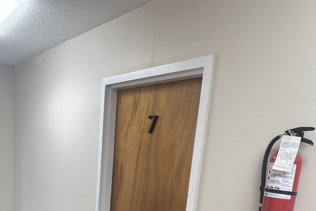 Un couloir avec une porte en bois portant le numéro 7, un extincteur fixé au mur et une poubelle noire.