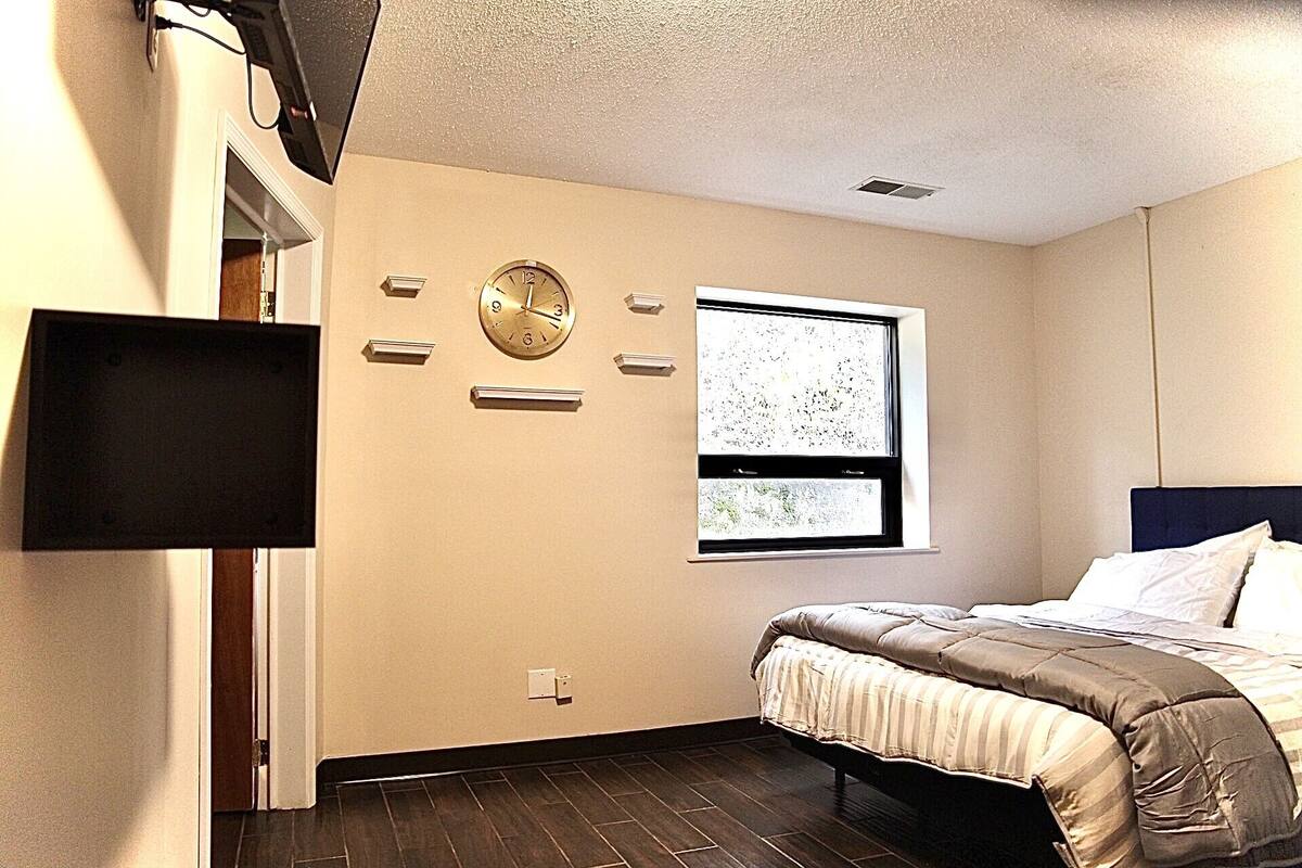 Une chambre à coucher avec un lit, une horloge murale, une fenêtre donnant sur un beau paysage et un téléviseur à écran plat.