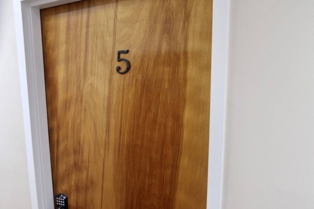 Une porte en bois portant le numéro « 5 », avec une poignée noire et un cadre blanc.