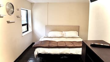 A bedroom with a bed, a clock, a window, and a remote control on a table.