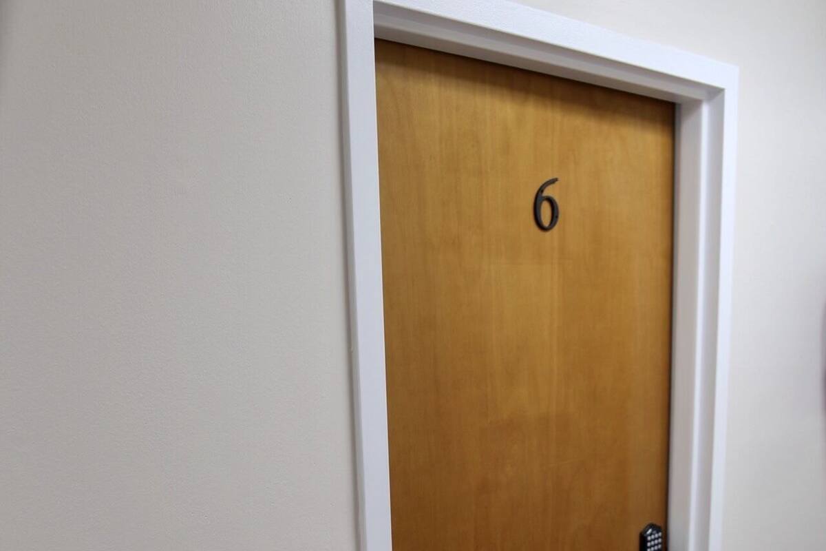Une porte en bois portant le numéro 6, avec des moulures blanches et une poignée noire.