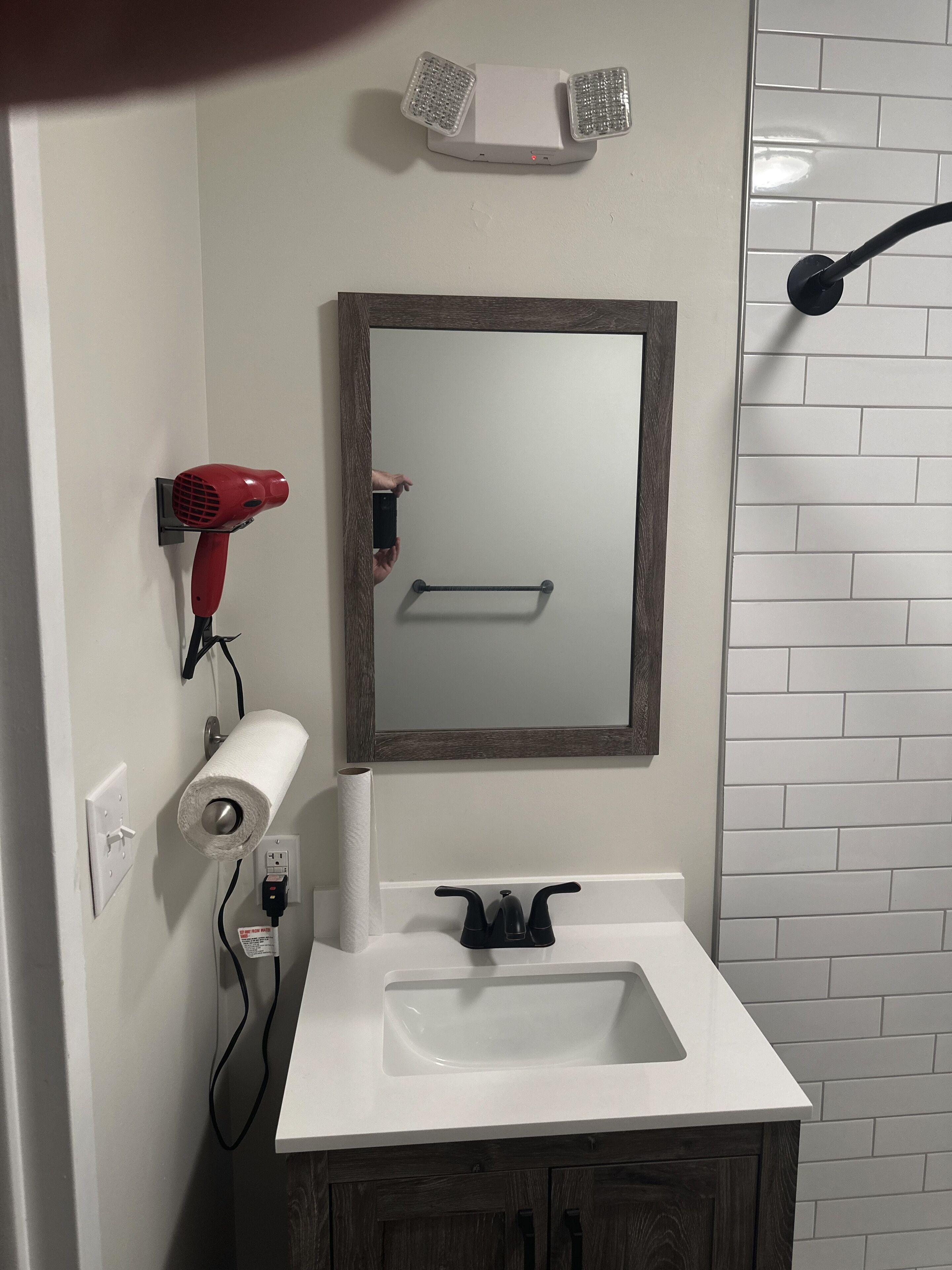A bathroom with a white sink, a mirror, a hairdryer, and a towel dispenser.