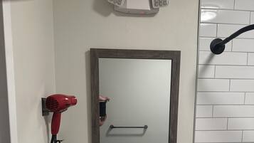 A bathroom with a white sink, a mirror, a hairdryer, and a towel dispenser.