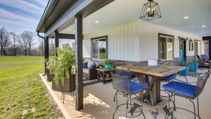 Un patio al aire libre con mesa y sillas de madera, una lámpara colgante y vistas del entorno.