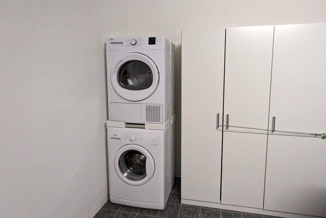 A stacked washer and dryer unit next to a white wardrobe with a metal handle.