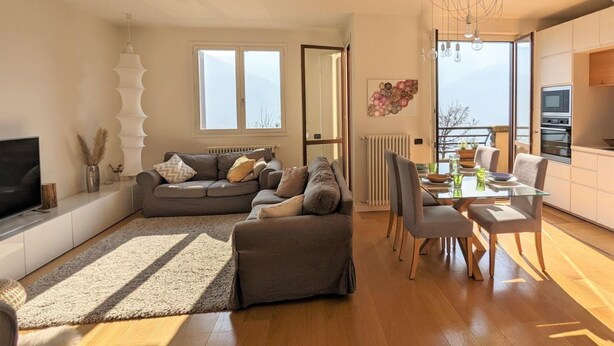 Un salon moderne avec un canapé, une table à manger et des chaises, un téléviseur et une grande fenêtre.