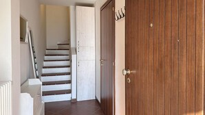 Un couloir avec un escalier menant à une porte blanche, une porte en bois et un porte-manteau.