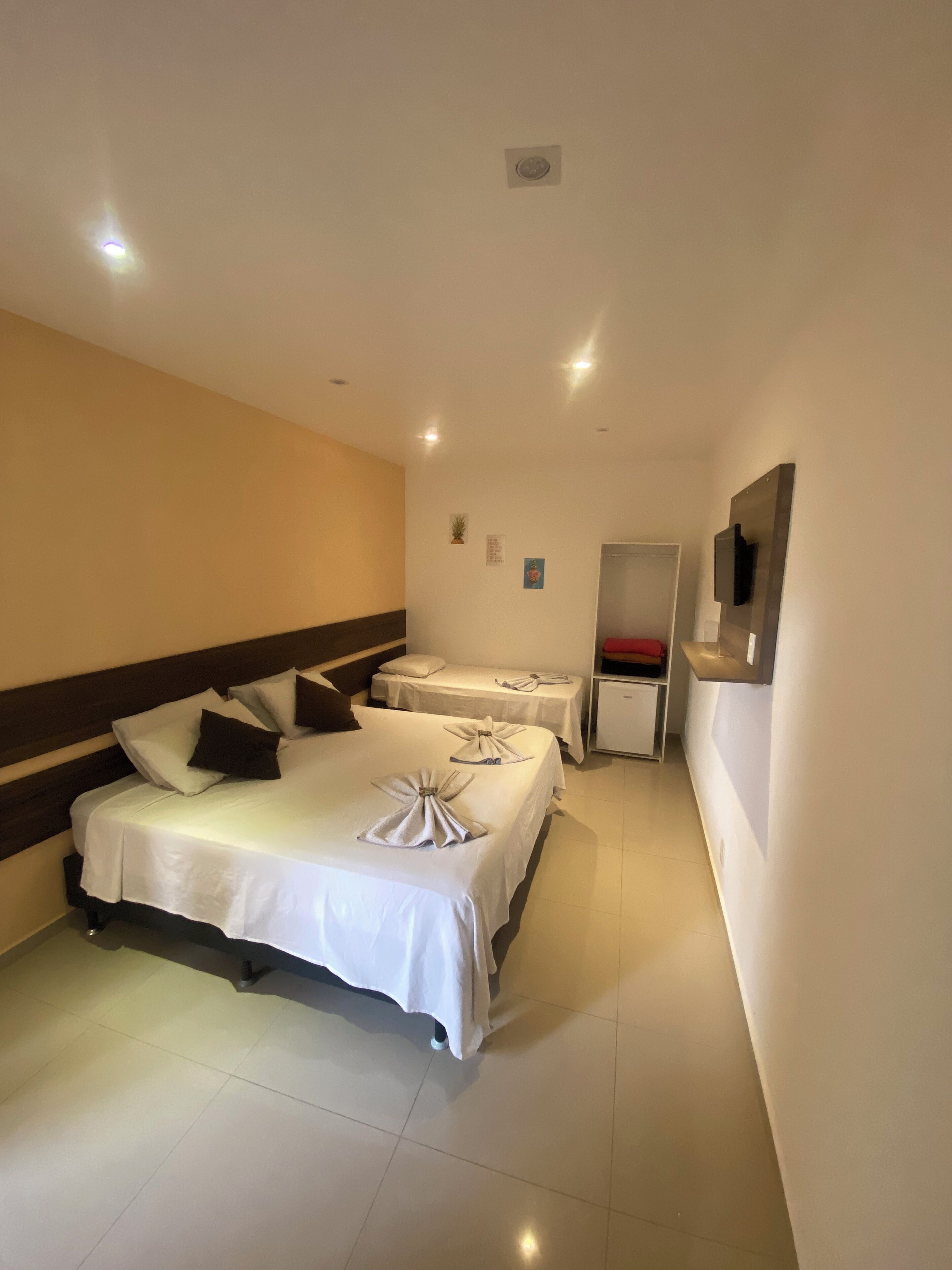 A hotel room with two beds, a TV mounted on the wall, and a small cabinet.