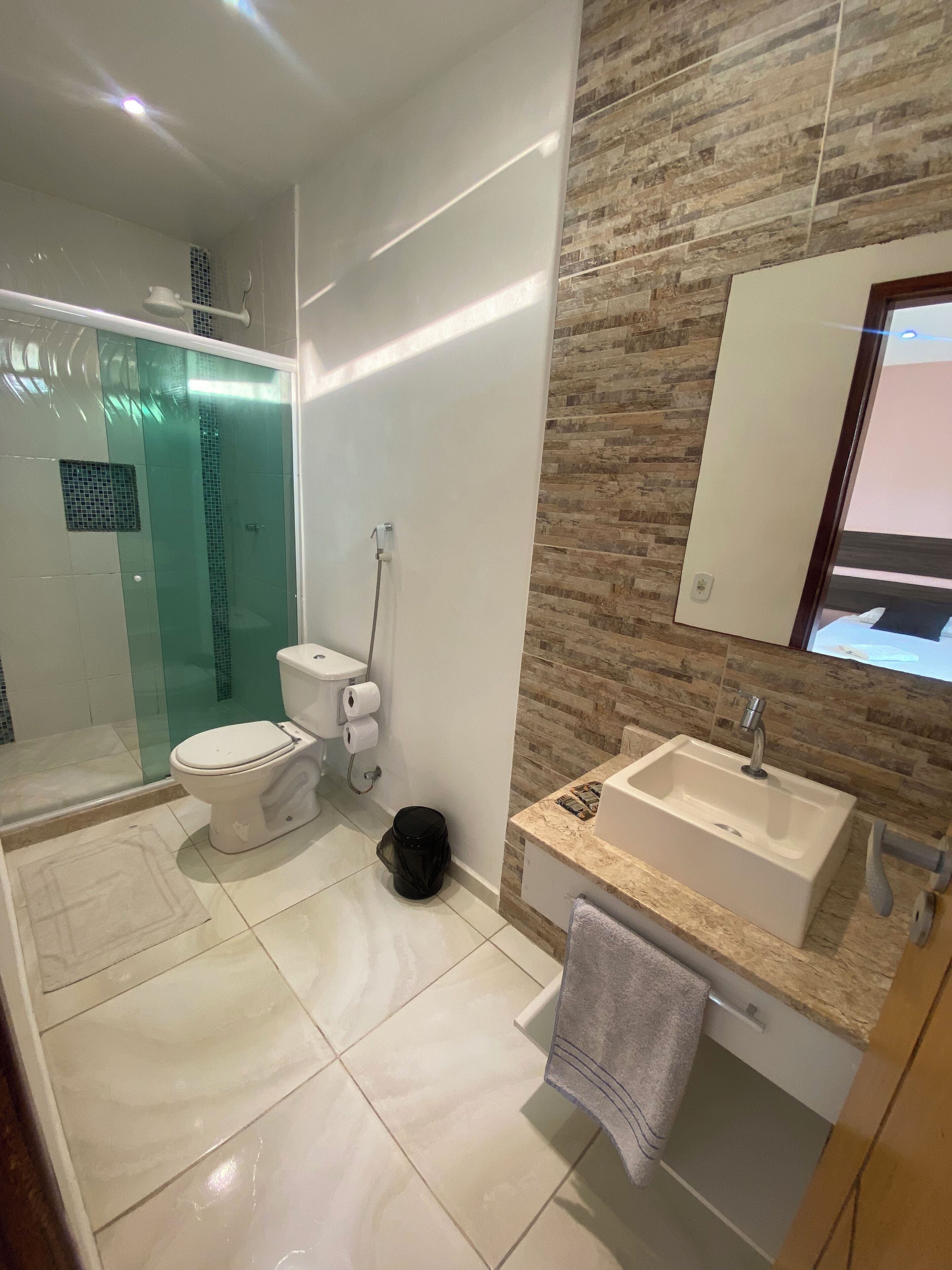A modern bathroom with a glass-enclosed shower, a toilet, and a sink with a towel hanging nearby.