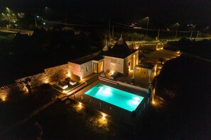 Een nachtzicht van een resort met een zwembad, stenen gebouwen en terrasjes.