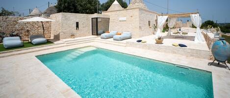 A pool area with stone walls, outdoor seating, and a pergola.