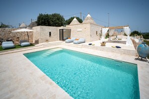Área de piscina com paredes de pedra, espaço para sentar ao ar livre e uma pérgula.