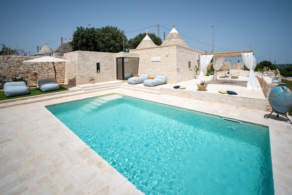 Un espace piscine agrémenté de murs en pierre, de sièges extérieurs et d’une pergola.