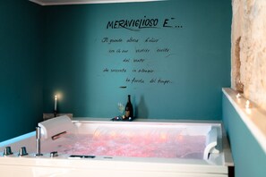 Une salle de bain avec une baignoire remplie d’eau, une bougie et une bouteille de vin posée sur le mur.