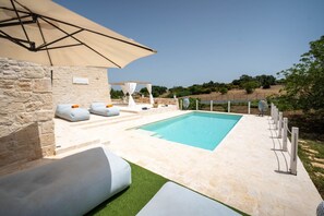 A pool area with a stone wall, lounge chairs, and an umbrella.