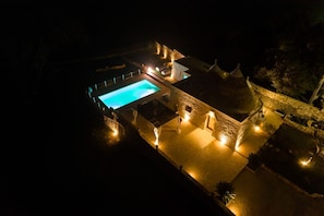 Vista nocturna de un resort con piscina, arquitectura de piedra e iluminación exterior.