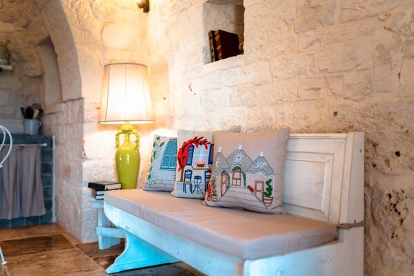 A stone-walled room with a bench and three cushions with house designs.