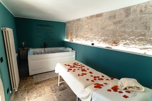 Une salle de spa avec un mur en pierre, une baignoire et une table de massage parsemée de pétales de rose.