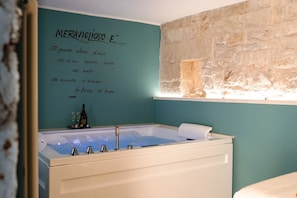 Une salle de bain moderne avec une grande baignoire, un mur en pierre et un mur de couleur turquoise orné d’une citation.