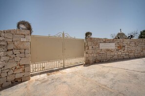 Une entrée fermée par un portail, avec un mur en pierre et une pancarte.