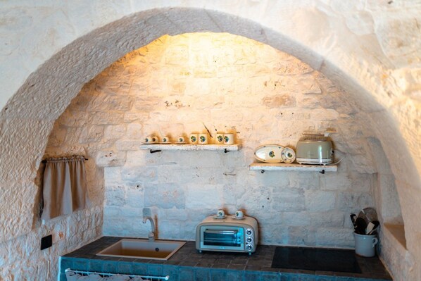 A stone-walled kitchen with a built-in oven, a sink, and a countertop with a toaster and a kettle.