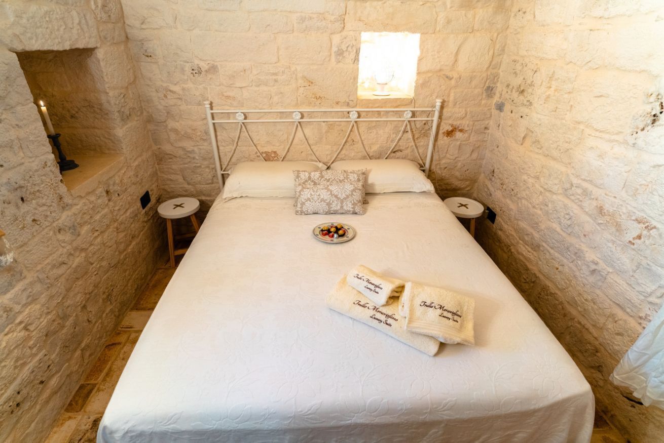 Une pièce étroite aux murs de pierre, avec un lit simple, une petite fenêtre et une bougie posée sur la table de chevet.