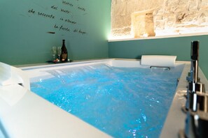 A hot tub with water jets, a bottle, and glasses on a table, and a wall with text in Italian.