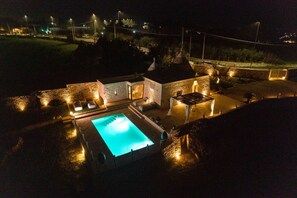 Vue nocturne d’un complexe hôtelier avec une piscine, des bâtiments en pierre et un éclairage extérieur.