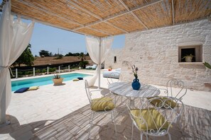 A covered outdoor area with a pool, stone walls, and outdoor furniture.