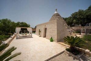 A stone building with a conical roof, a covered outdoor seating area, and a pool in the background.
