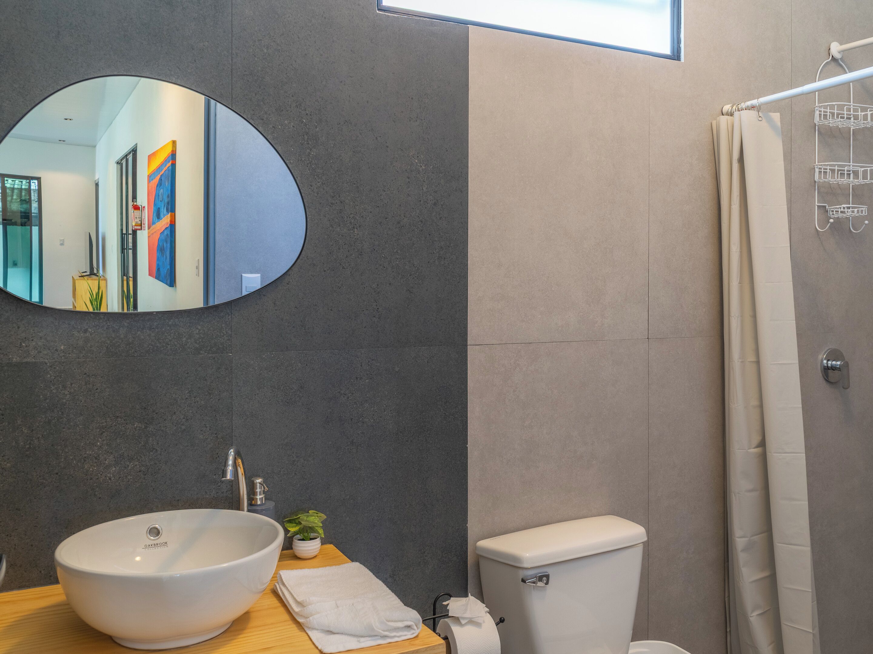 Een moderne badkamer met een grote, ovale spiegel, een witte wastafel, een toilet en een douchegordijn.