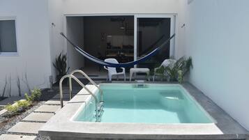 A swimming pool with a hammock, a patio area, and a sliding door leading to an interior space.