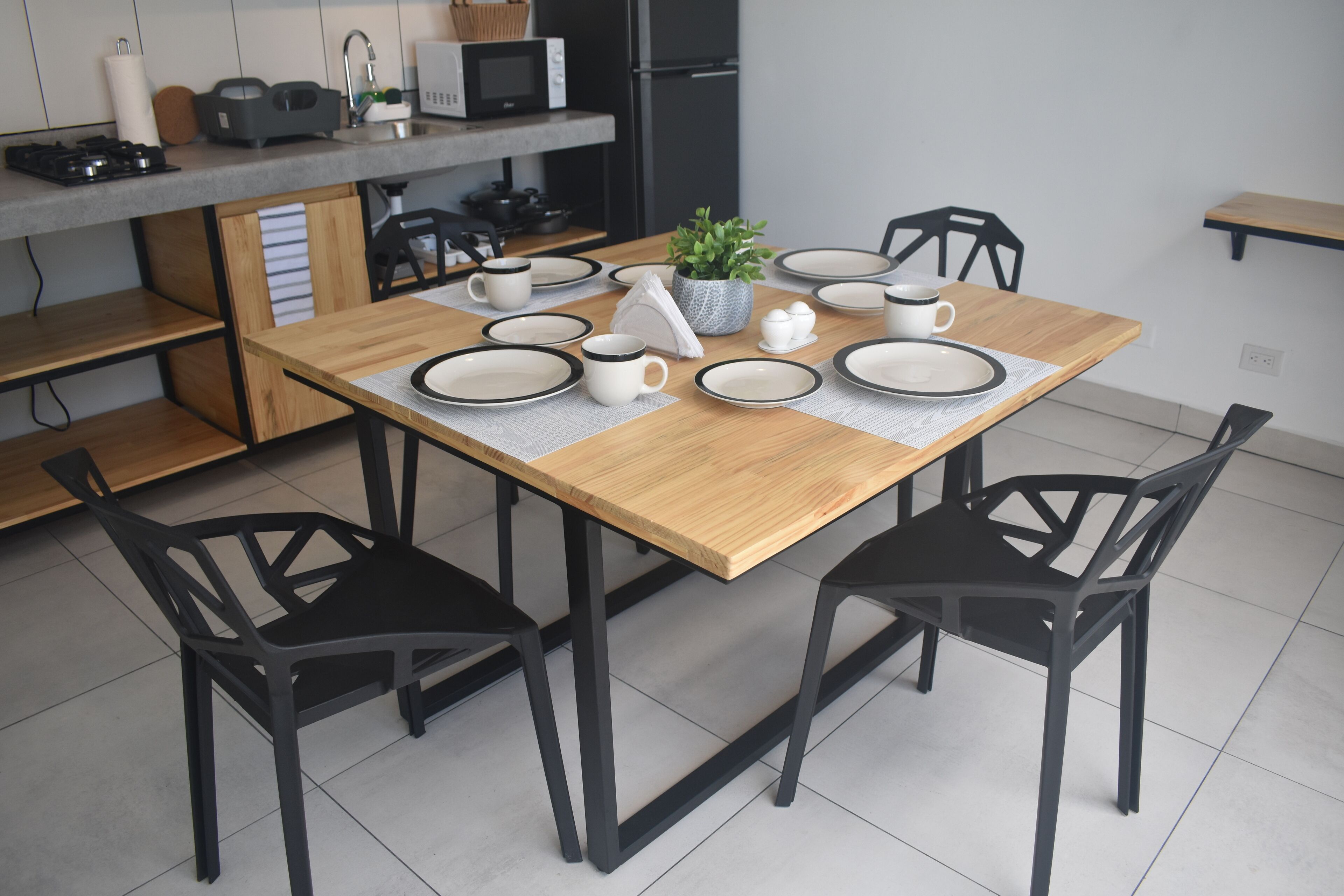 A modern kitchen with a wooden dining table set for four, black chairs, and a microwave above the counter.