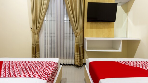 A hotel room with two beds, a TV mounted on the wall, and a shelf above the beds. - OYO 3763 Oq Guest House Syariah (Malang)